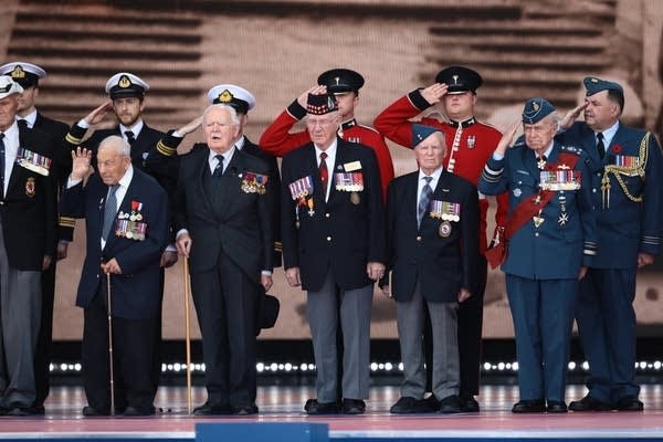 Veterans salute from the stage as they attend the D-Day commemorations.