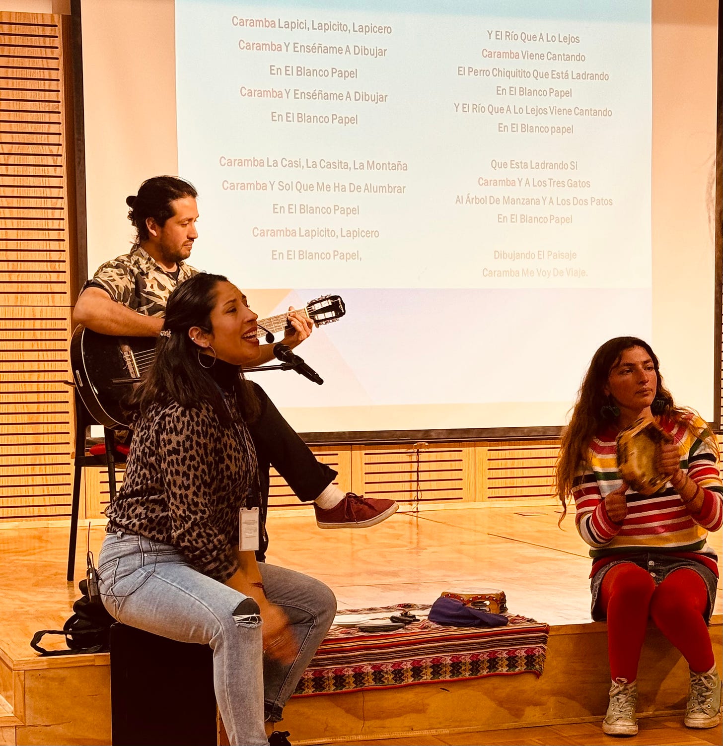 Una mujer toca el cajón, otra la pandereta y un muchacho la guitarra. Al fondo, la letra de una cueca. Foto propia.