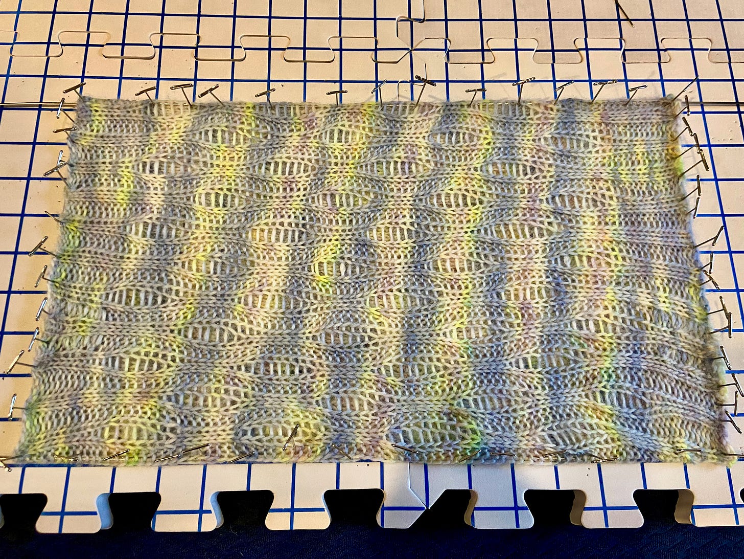 The Little Creek Cowl blocked and pinned down on foam blocks. The yarn is variegated.