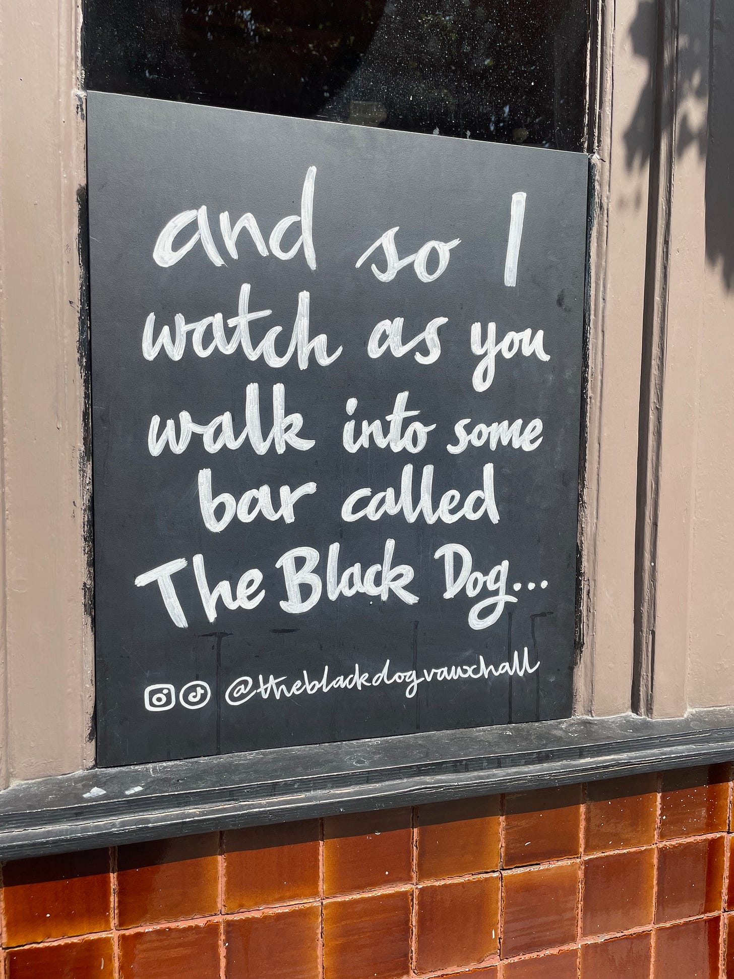 chalkboard outside pub reading "and I watch as you walk into some bar called the black dog"