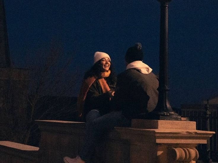 This may contain: two people sitting on a stone wall next to a street light at night with the moon in the sky