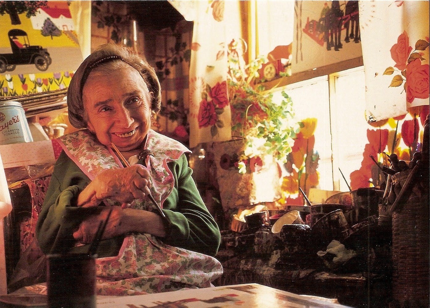 Foto de Maud lewis con un pincel en la mano en su casa de Canadá, toda llena de sus dibujos y flores