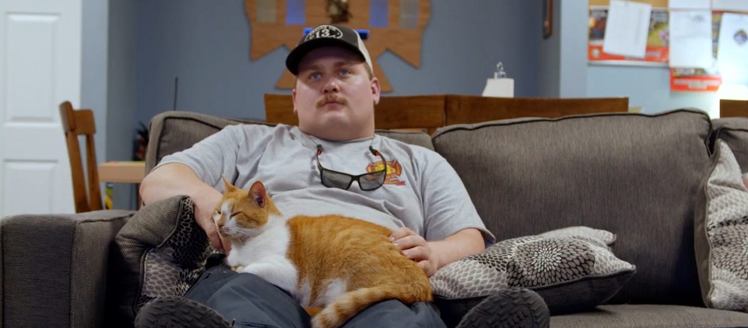 A man sitting on a couch with an orange and white cat on his lap.