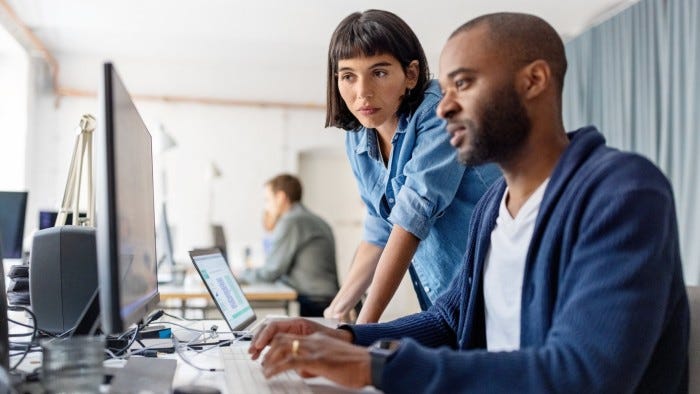 Two business people looking at desktop computer monitor and discussing new programme codes