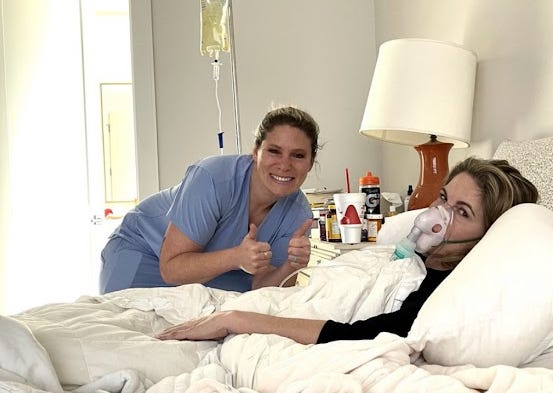 A 2022 photo of Mary Talley Bowden bedridden at home with COVID-19 whilst wearing an oxygen mask and hooked up to fluids. Her fellow anti-vax doctor is posing with two thumbs up and a big smile over her near-dead corpse.