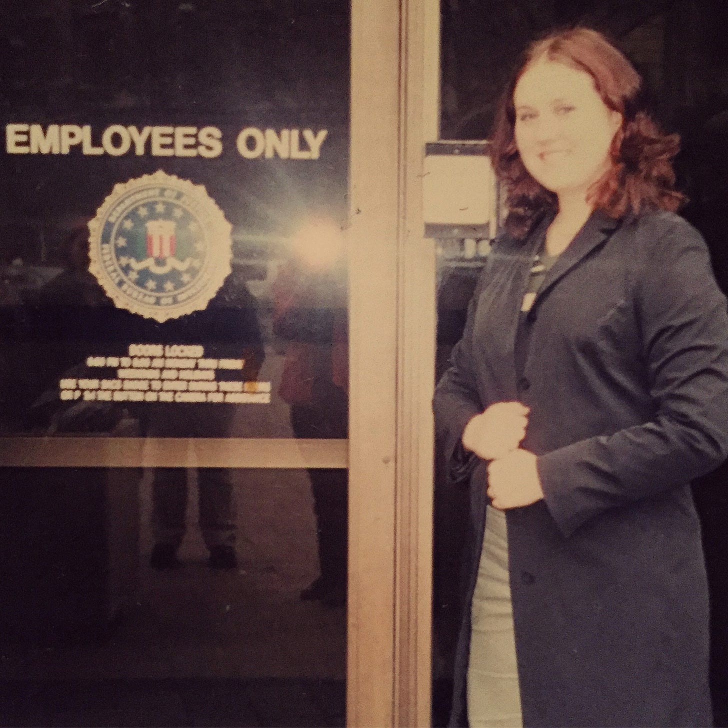 Me as a teen in front of an "Employees Only" door at the FBI Building in Washington, DC. I am wearing a black trench coat and have dyed auburn hair.
