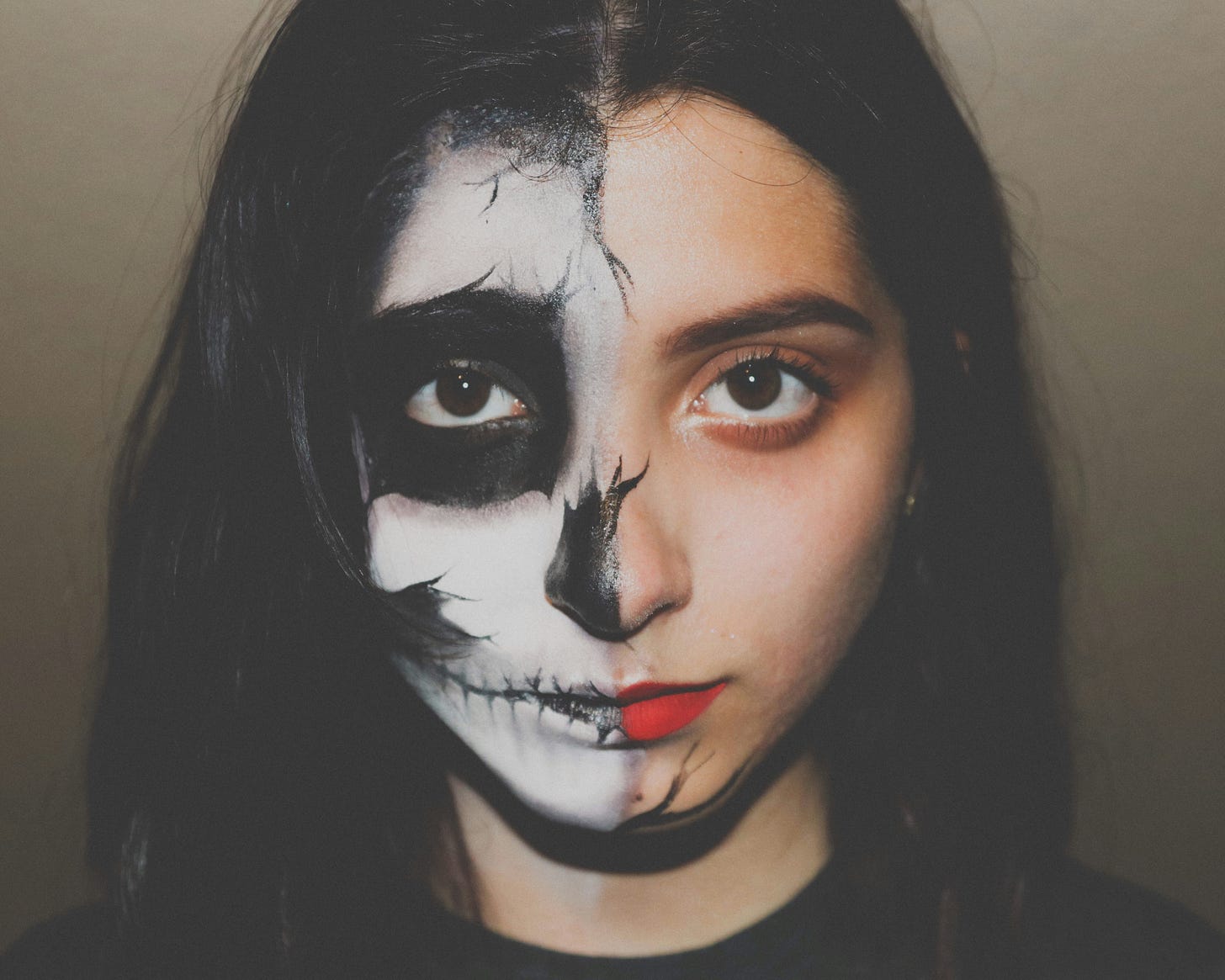 A teenager with long black hair and scary halloween makeup on one side of their face. A teenager with long black hair and scary halloween makeup on one side of their face.