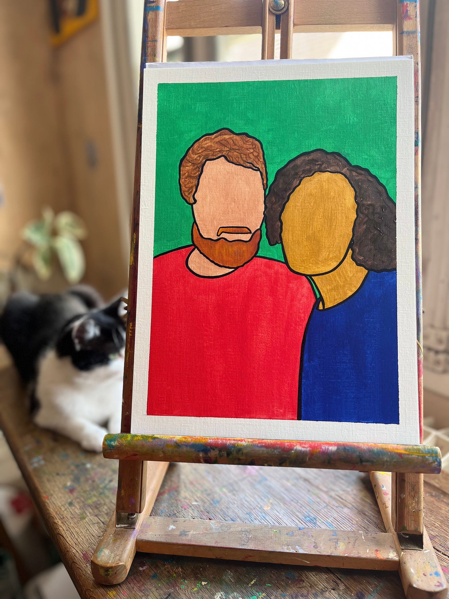 Two faceless portraits on a green background on an easel near a cat
