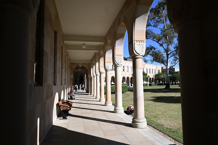 A walkway next to a building featuring curved stone archways and a bench. The walkway is empty.