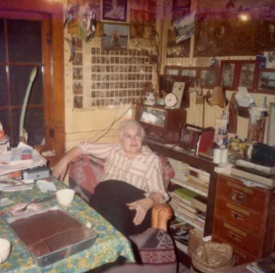 Color image of Dorothy Molter sitting at the kitchen table of the Point Cabin, Isle of Pines, Knife Lake, Boundary Waters Canoe Area, ca. 1970s.