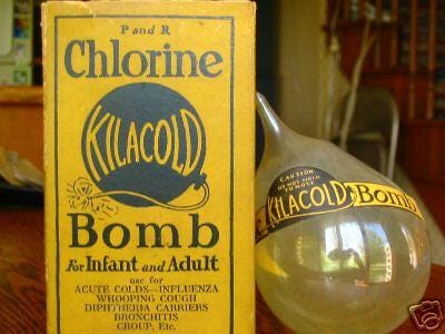 A yellow cardboard box with a picture of a bomb with the word 'Kilacold' on it. Next to the box is a yellowish glass bulb with a label round it saying 'Kilacold Bomb'.