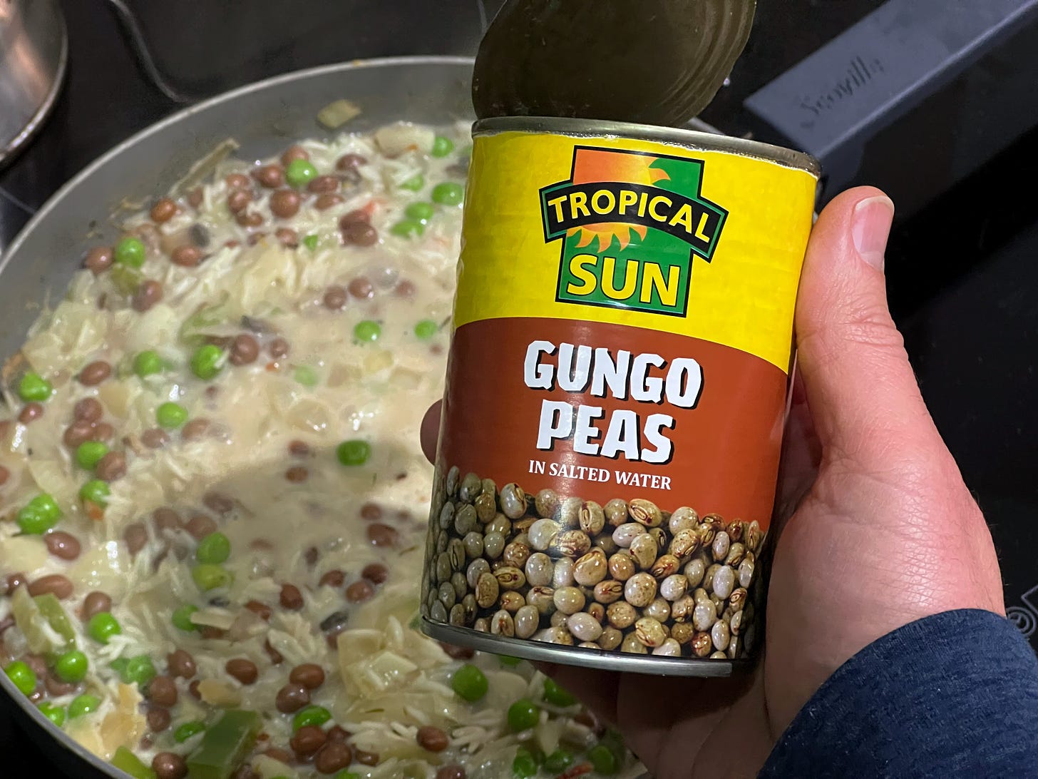 A tin of Gungo peas being held over a simmering pan.