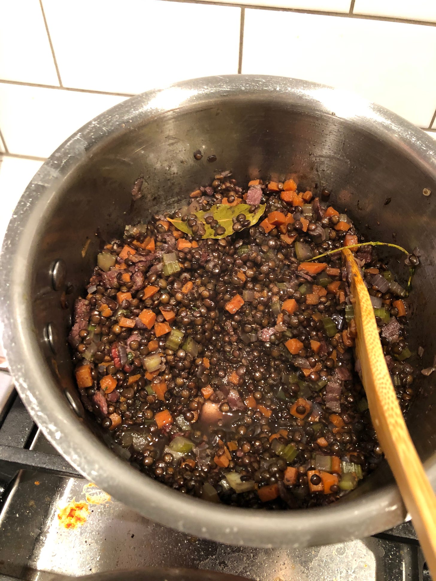 A pot full of beluga lentils, chopped bacon, celery, and carrots cooking down into a ragout