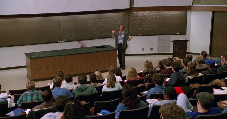 A professor standing at the front of a classroom, lecturing to a group of students seated in rows in front of him.