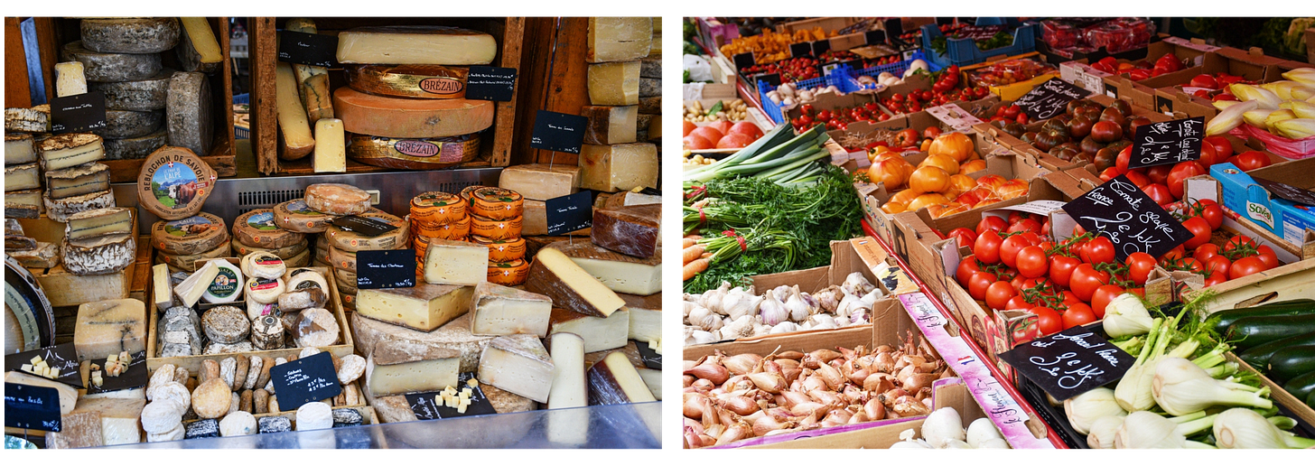 Market scene in Annecy, France, featuring an assortment of French cheeses displayed in wooden crates on the left and a colorful variety of fresh vegetables, including tomatoes, leeks, carrots, and garlic, on the right.