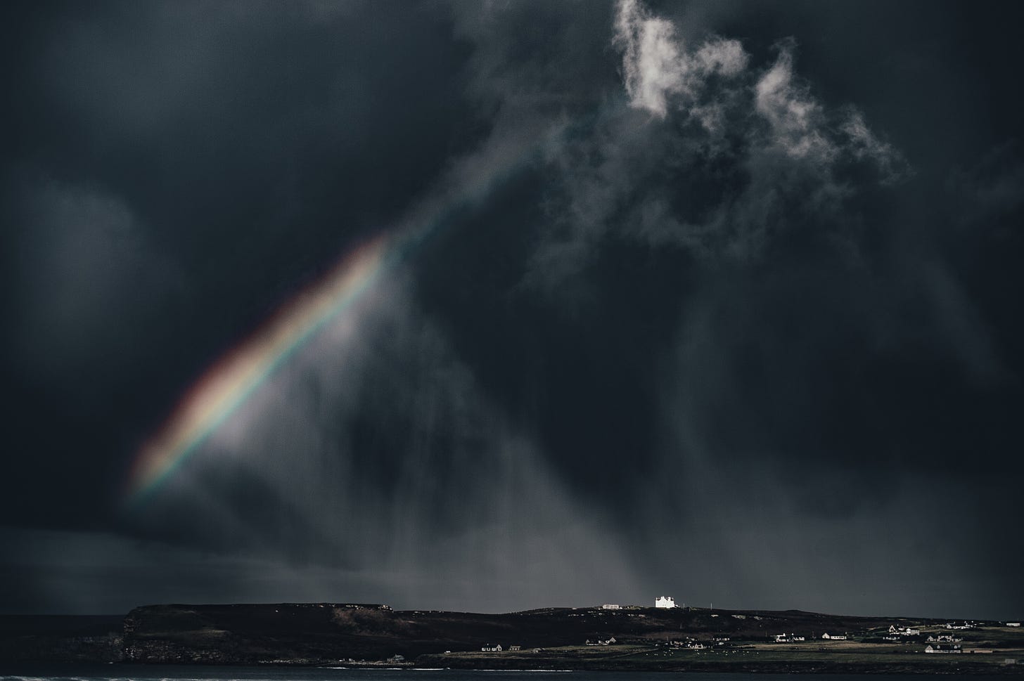 Light and a faint rainbow appearing through dark clouds
