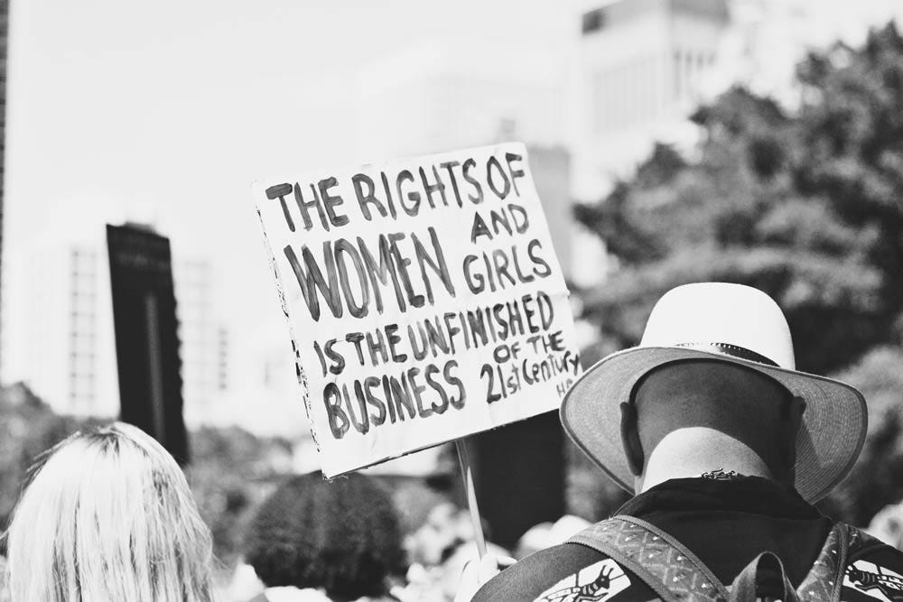 Protest sign reading "the rights of women & girls is the unfinished business of the 21st century."