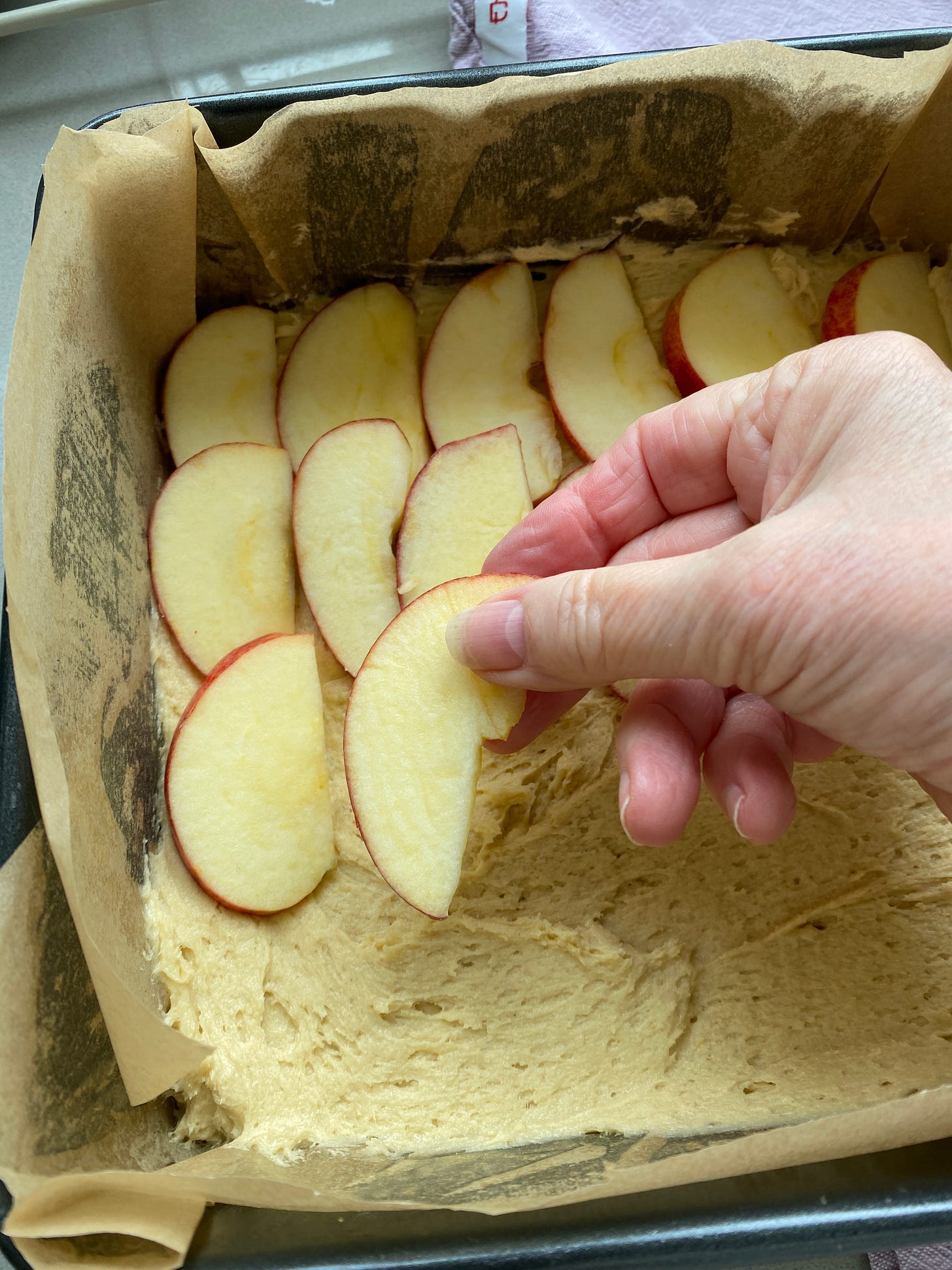 Adding a layer of sponge mixture and a layer of apple slices into the prepared cake tin.