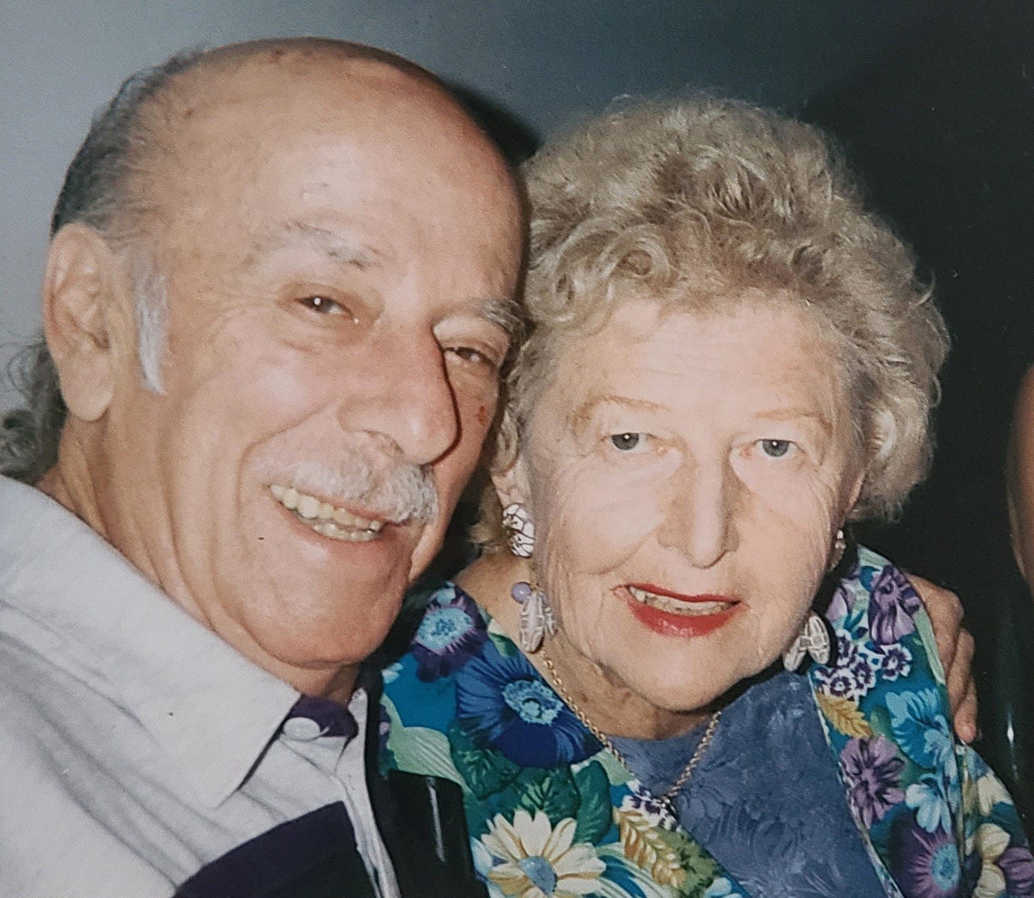 A color photograph of an elderly couple smiling together into the camera.