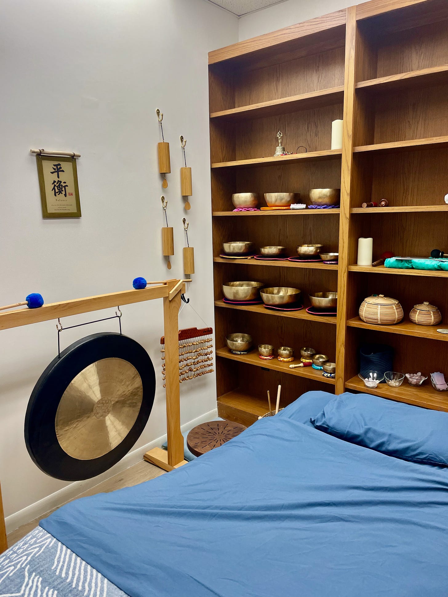 a large gong and several sound healing instruments on bookshelves are near a bed with a blue covering