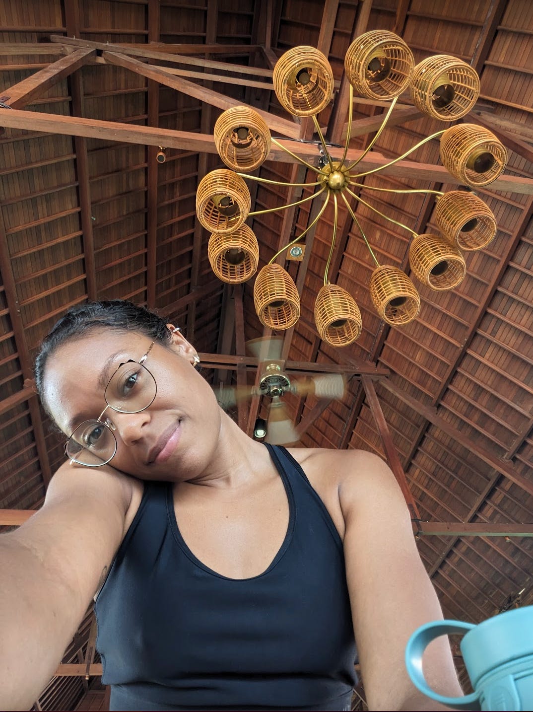 Nathalie is sitting under a wooden chandelier. She is smiling slightly at the camera while one side of her face is leaning on her shoulder.