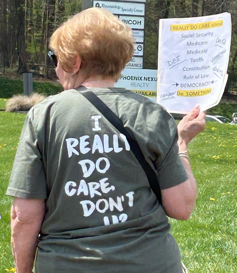 A woman in sunglasses wearing a green t-shirt resembling the infamous Melania coat - except the text reads "I really do care, don't u?" She is holding a piece of paper that says "I really do care about Social Security Medicare Medicaid Tariffs Rule of Law Democracy DO SOMETHING" A woman in sunglasses wearing a green t-shirt resembling the infamous Melania coat - except the text reads "I really do care, don't u?" She is holding a piece of paper that says "I really do care about Social Security Medicare Medicaid Tariffs Rule of Law Democracy DO SOMETHING"