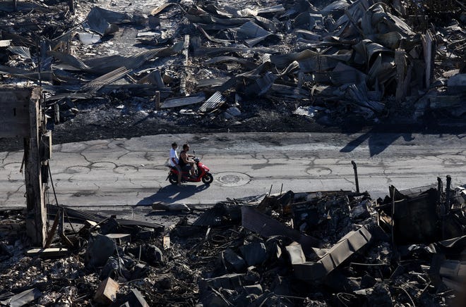 In an aerial view, two men ride a scooter by businesses that were destroyed by a wildfire on Aug. 11, 2023, in Lahaina, Hawaii.