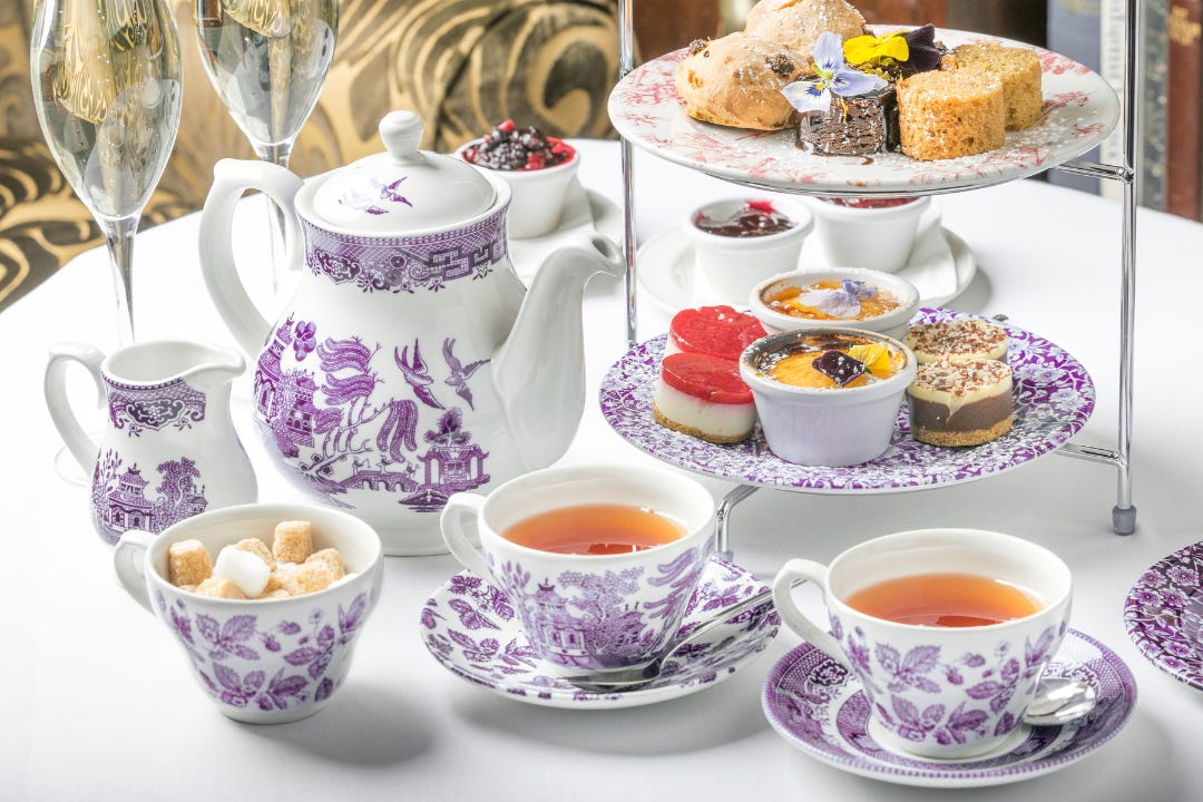 pretty table with white linens and full tea service, plus a multi-tiered tray of delicious treats