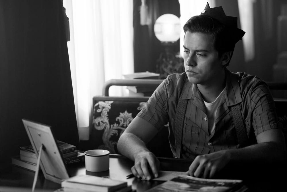 Jughead looking at a photo on a desk in black and white.