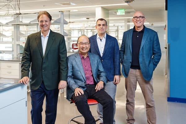 Three men are standing and one is seated inside a science lab.