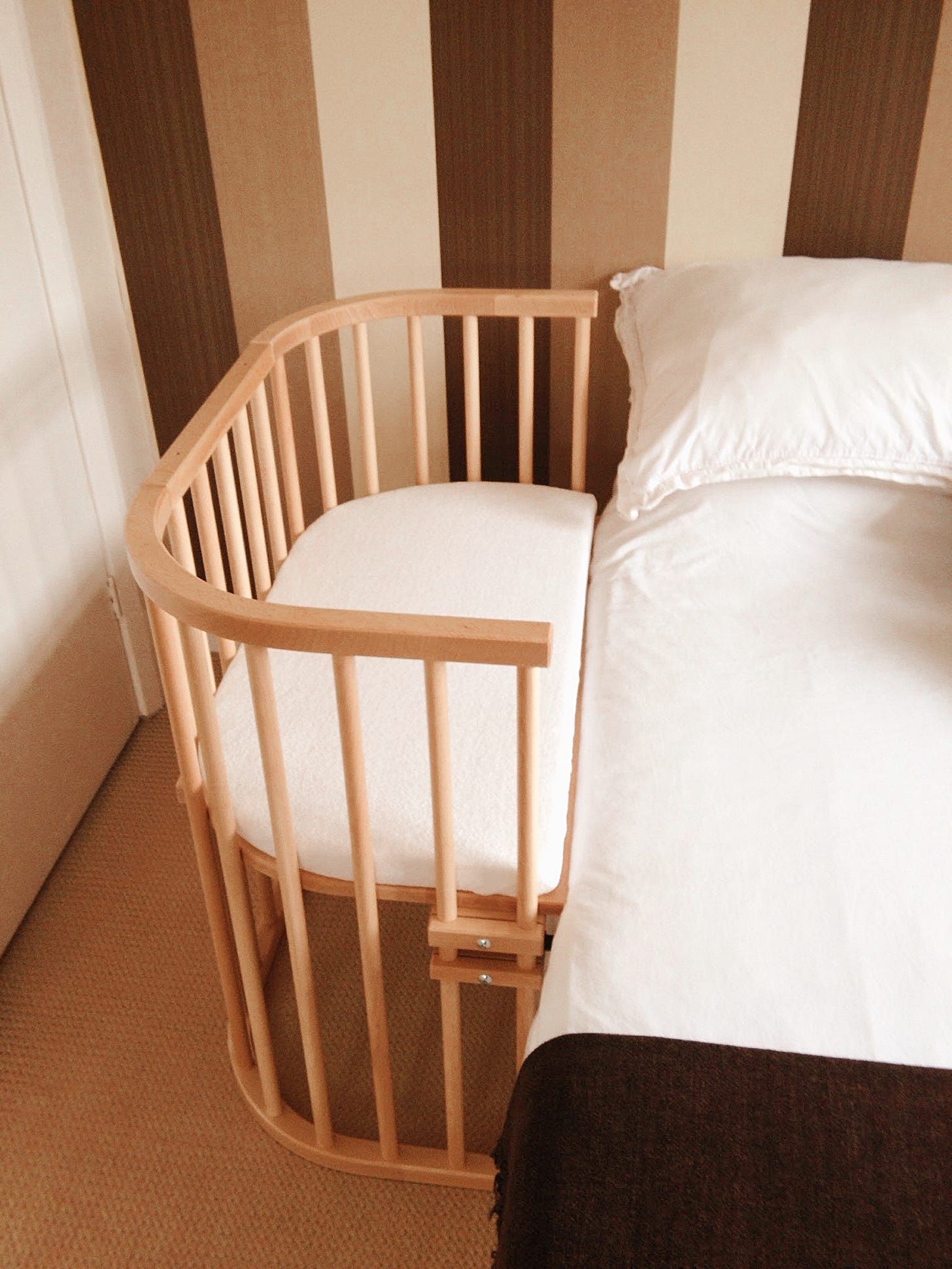 A bedside cot is alongside a bed with white linen