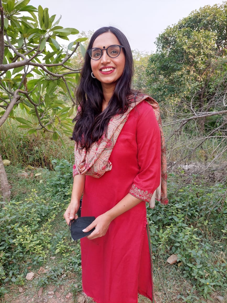 Shreyasi in a red dress, smiling at the camera amidst greenery
