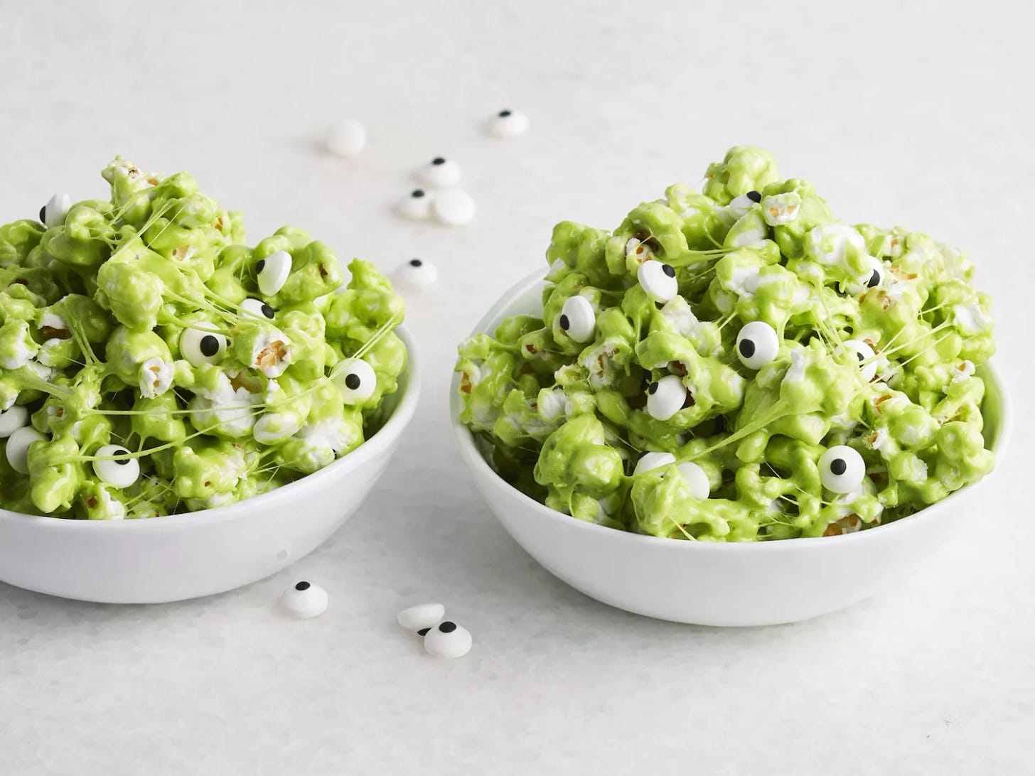 green-colored sticky popcorn with candy eyeballs in white bowls