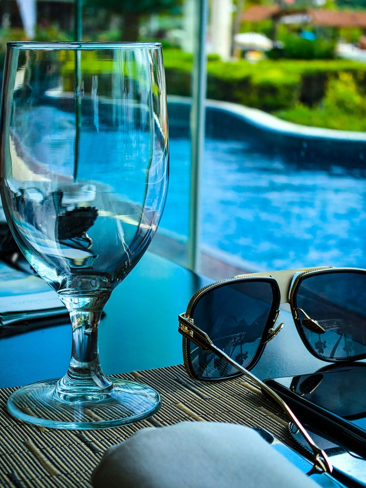 A blue water pool, an empty glass and a pair of sunglasses