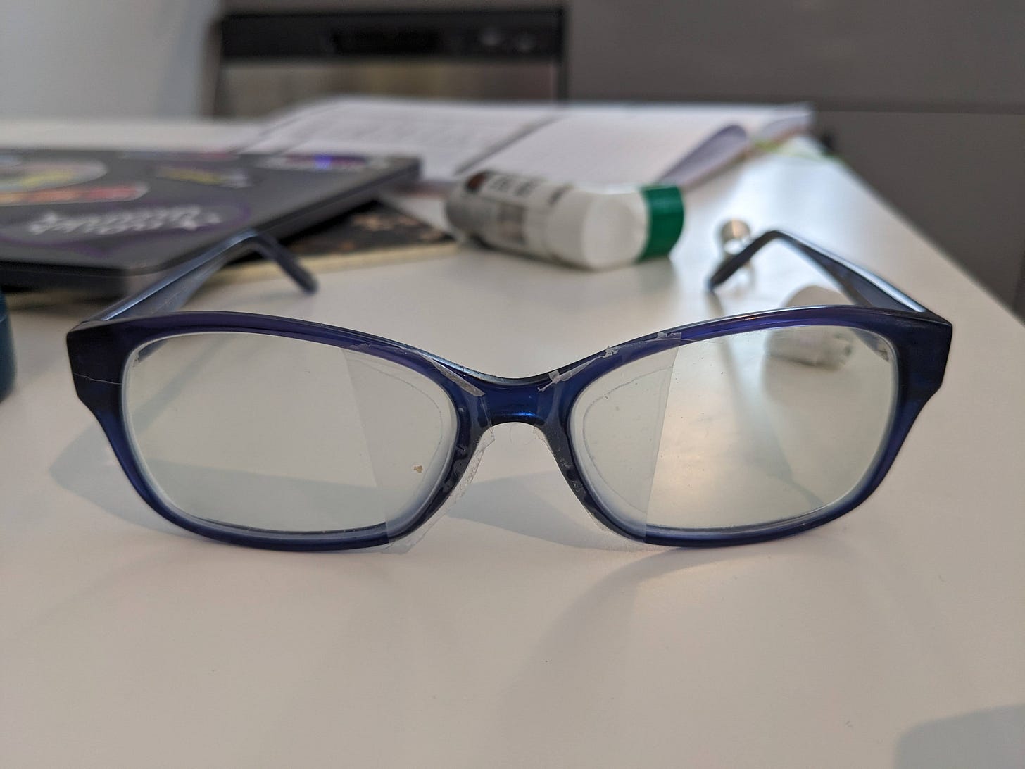 A pair of blue glasses sitting on a white table with transparent tape on the inner corners. 