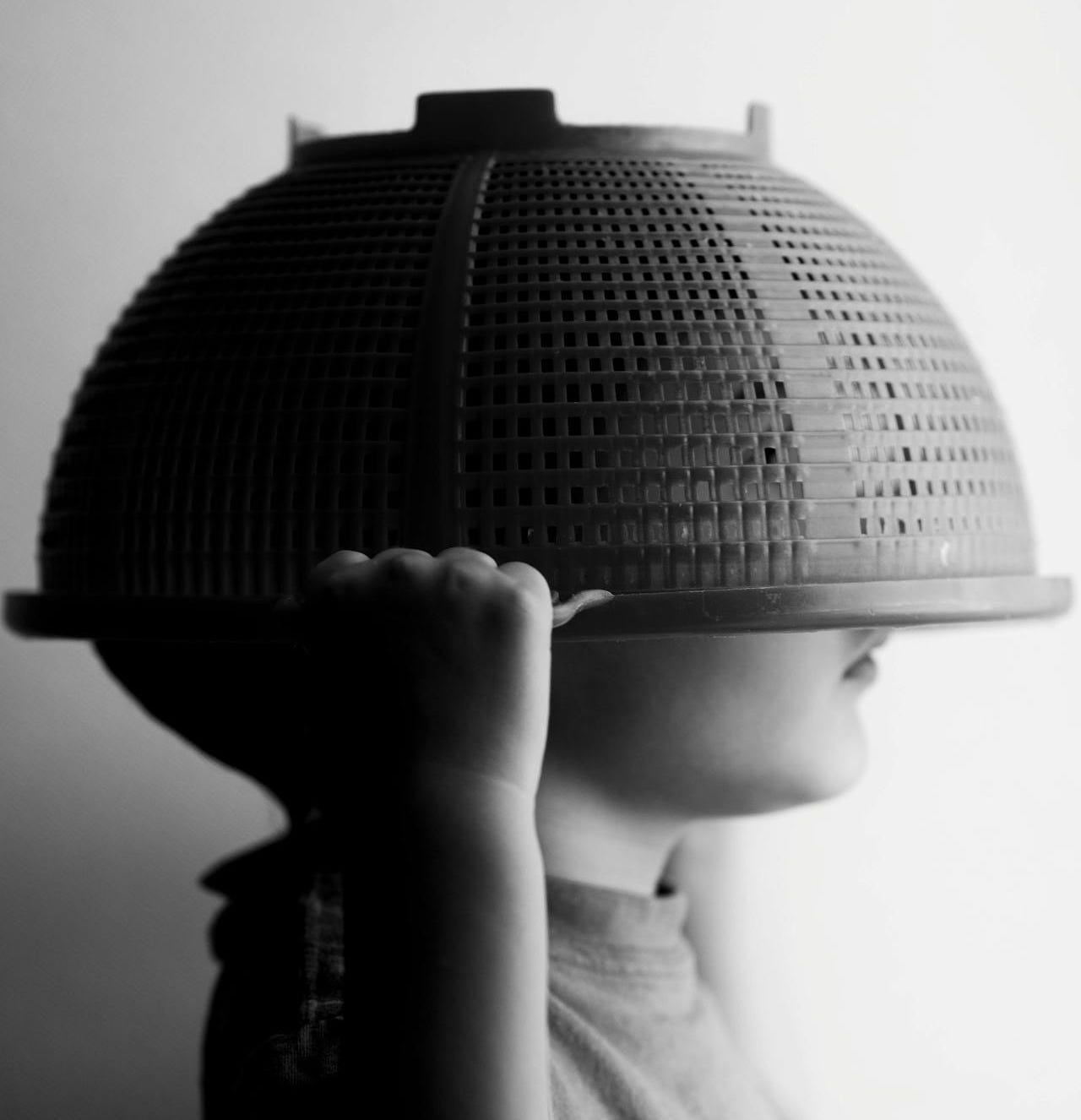 A small boy holding a colander over his head