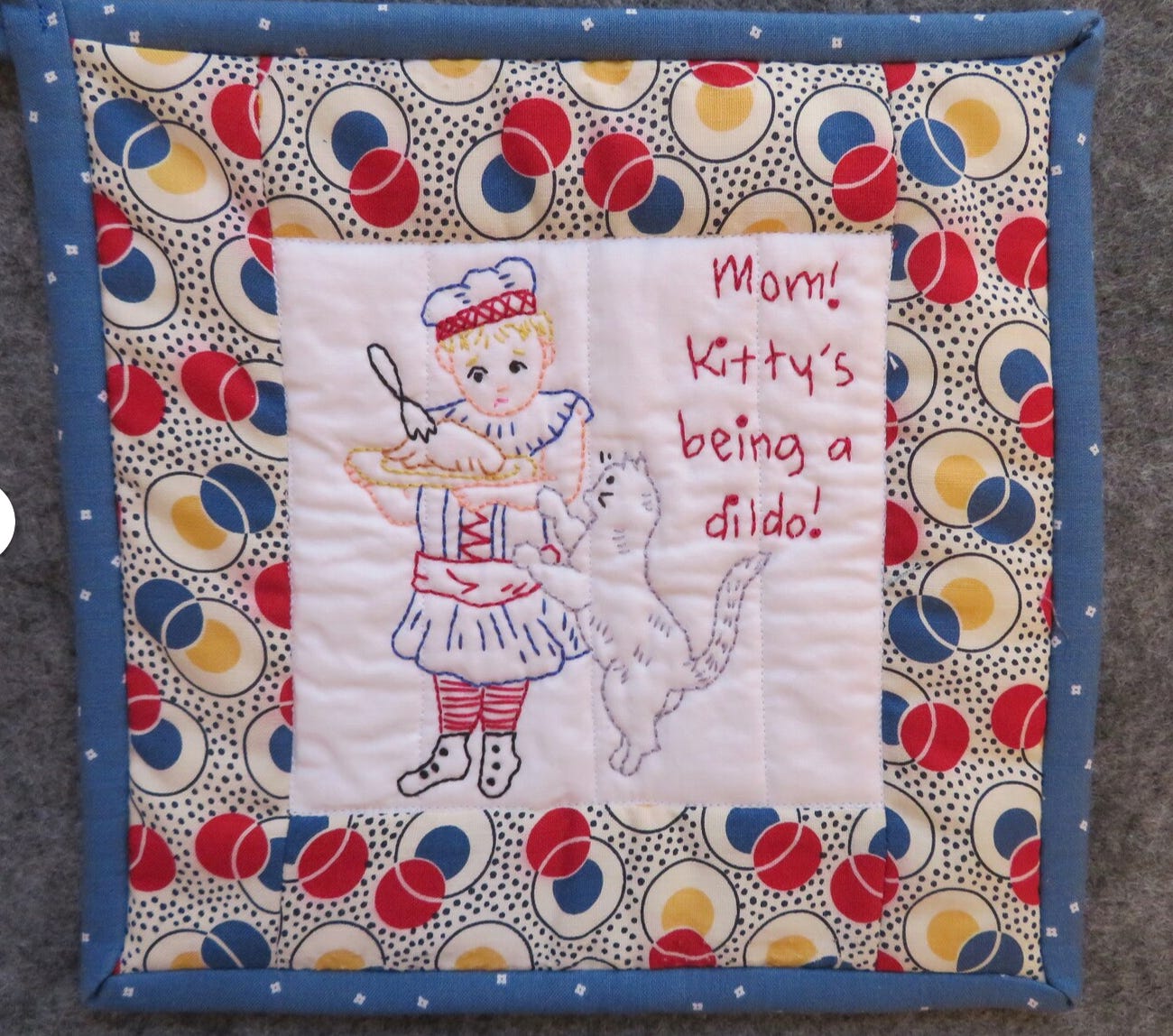 Potholder: kid and cat, cross-stitched: "Mom! Kitty's being a dildo!"