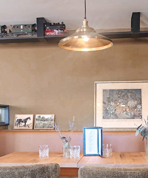 A pub interior with green walls, seating with art prints next to it, and a train on a black track on the ceiling