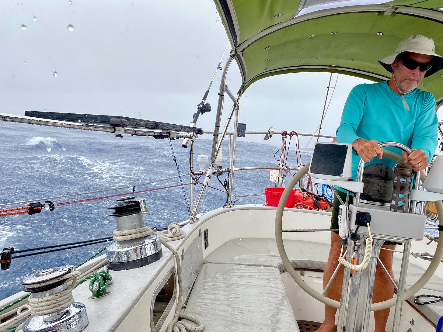 Image of a man at the helm of a sailboat on the ocean, while a squall pours heavy rain on the cockpit
