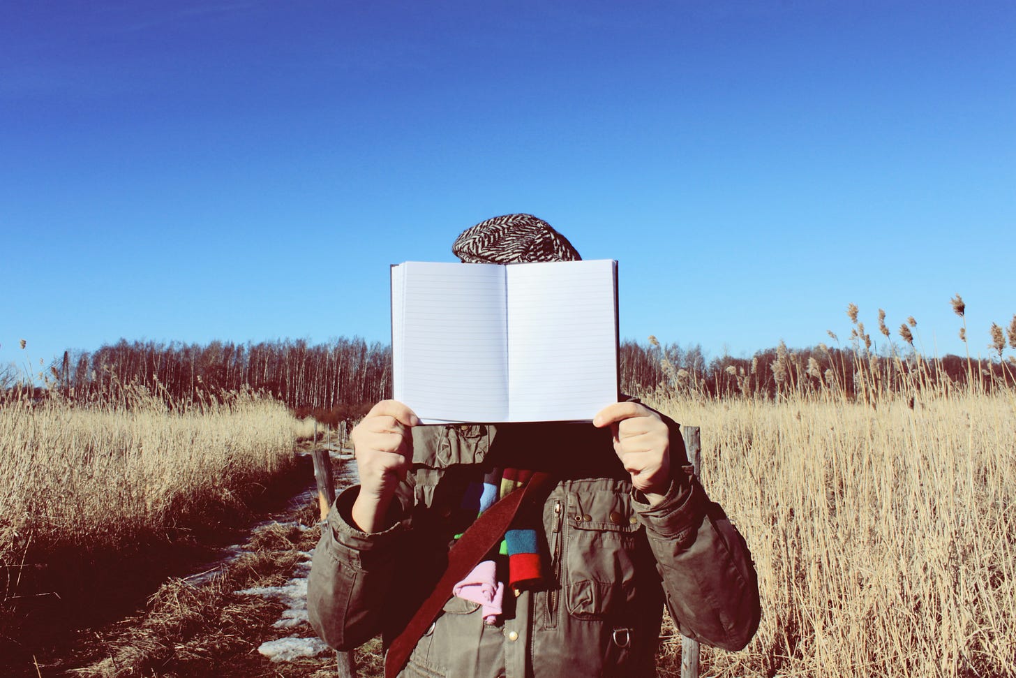 Person in a field with an open book, facing the viewer, showing blank pages