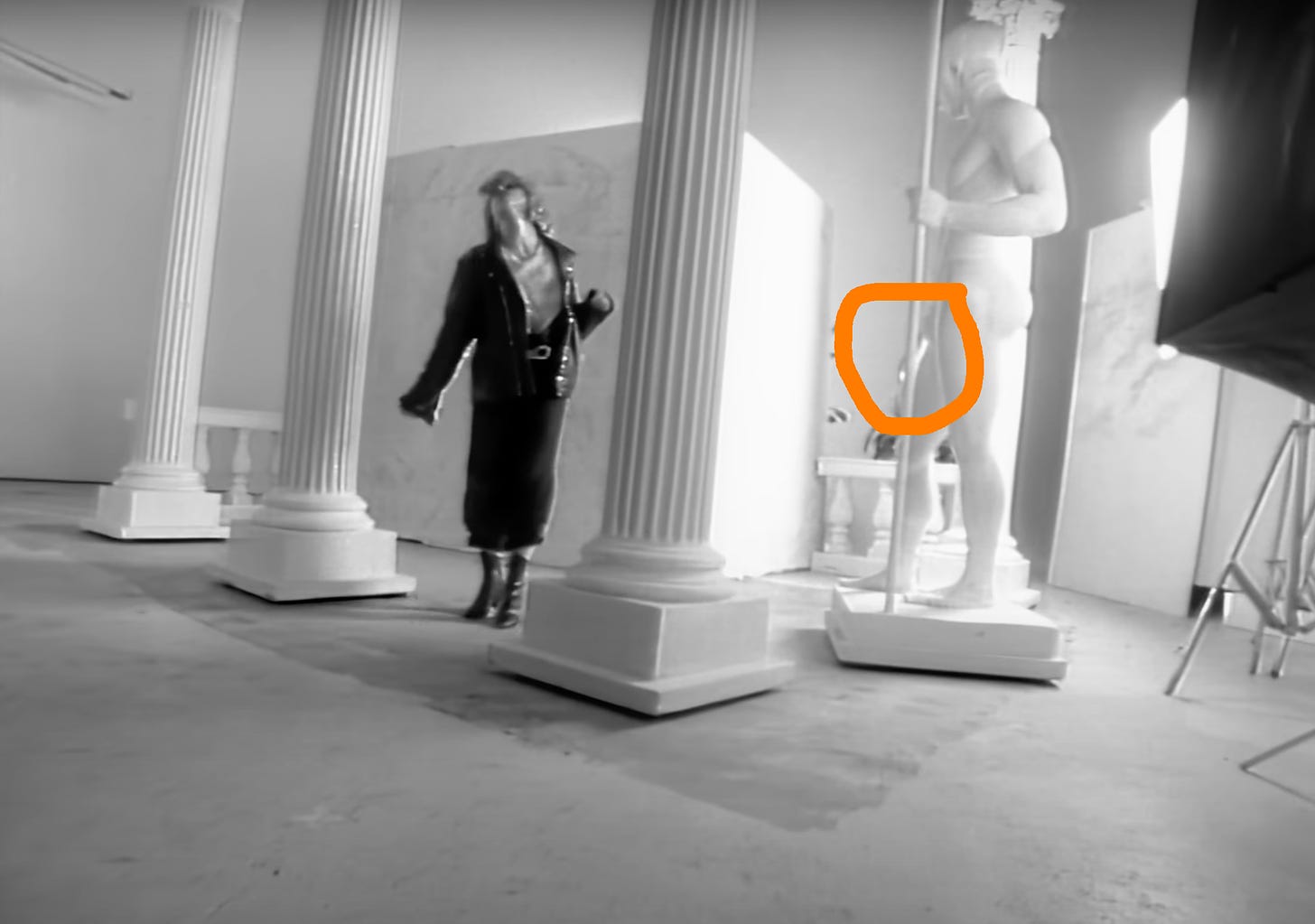 Still from the Borderline video featuring Madonna dancing around a photographic studio with Greek columns and a statue with what looks like a large appendage on the front of its body which is circled in orange so that readers can see it properly