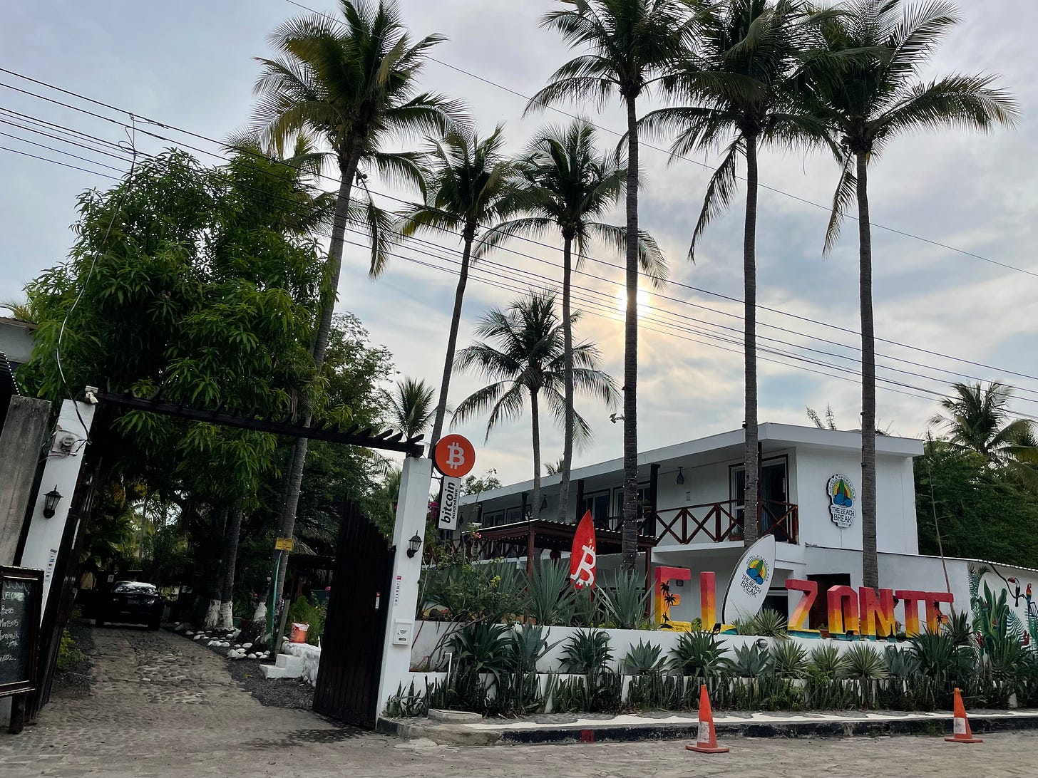 Entrance to a hotel lined with palm trees, and various signs with the Bitcoin logo around the entrance