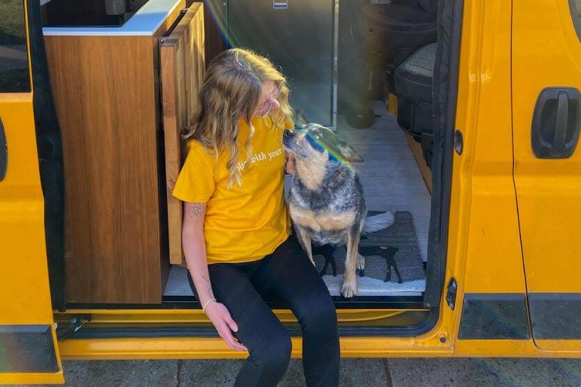 Scout the blue heeler and Haley the human sit on the sliding door step of our converted camper van, looking at each other