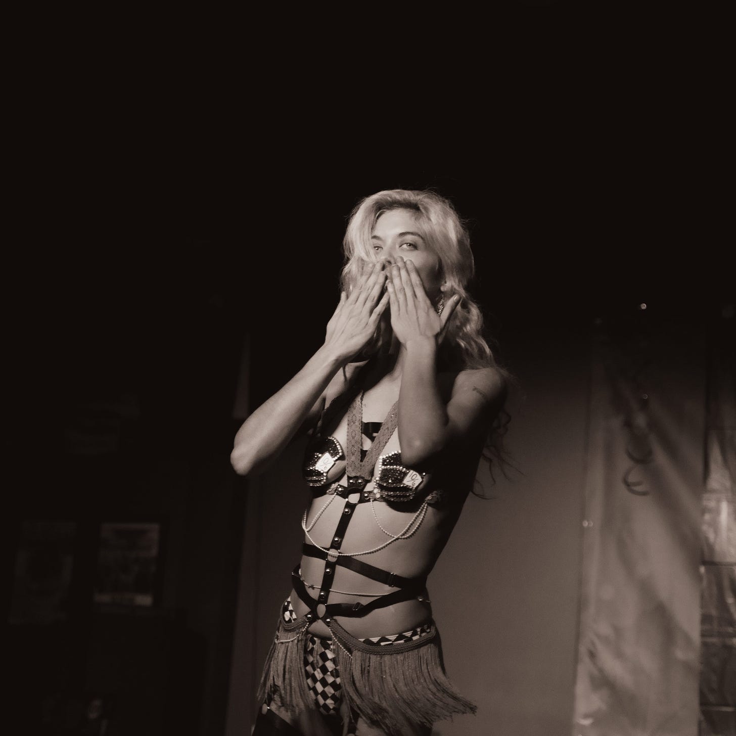 Black and white photo of Flat Baroque organizer and model Gigi wearing a burlesque outfit with her hands over her mouth in an expression of delight.