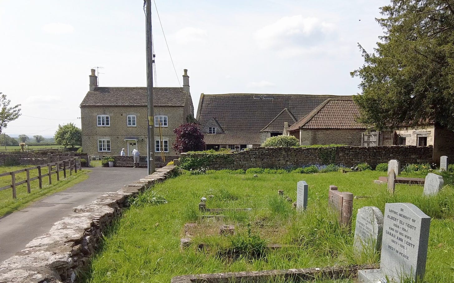 Church Farm and the medieval barn to its right. In the foreground are some of the graves in the churchyard. Image: Roland's Travels
