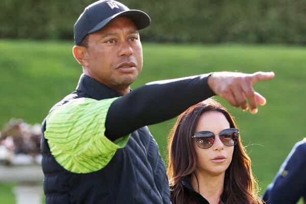 Tiger Woods, left, stands next to a woman on a golf course and points with his right hand. 