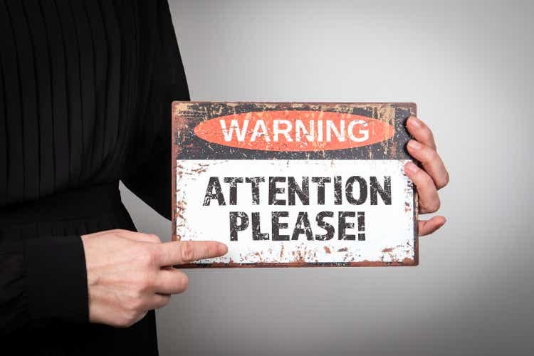 Attention please. Warning sign in a woman"s hands on a light background