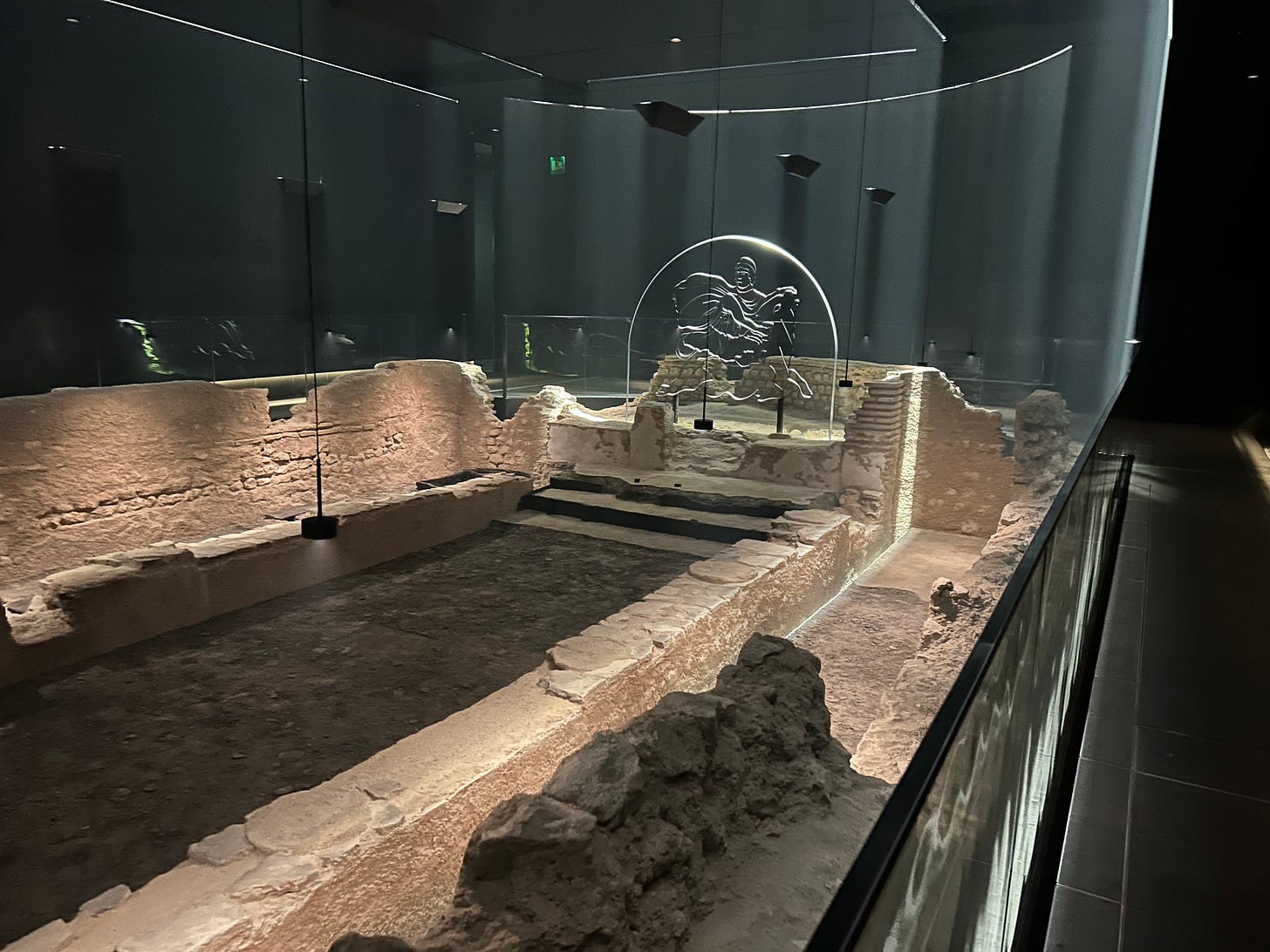 A reconstructed roman temple inside a dark space with black walls. There is a Perspex image of a roman deity at the end of a long brick construction.