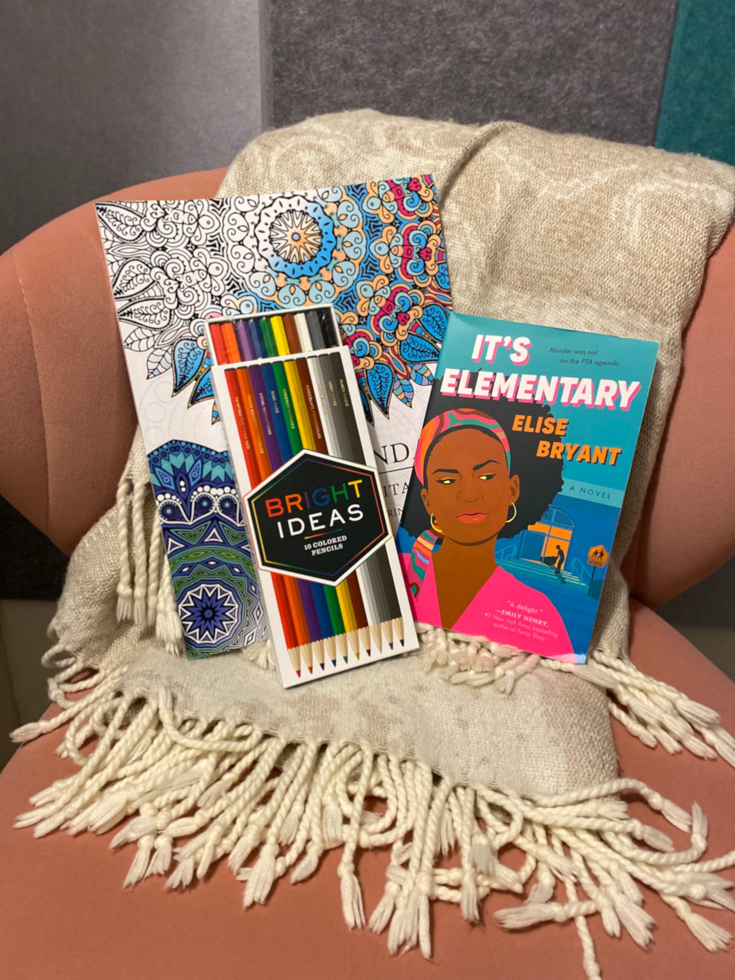 colored pencils, coloring book and novel pictured on chair