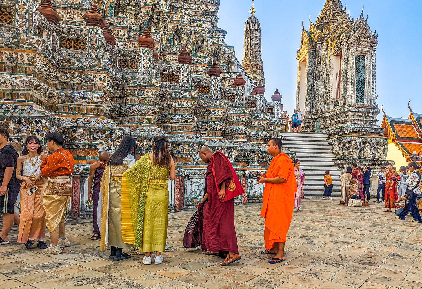 A group of young people dressed in colorful traditional Thai clothing, as well as two monks. 